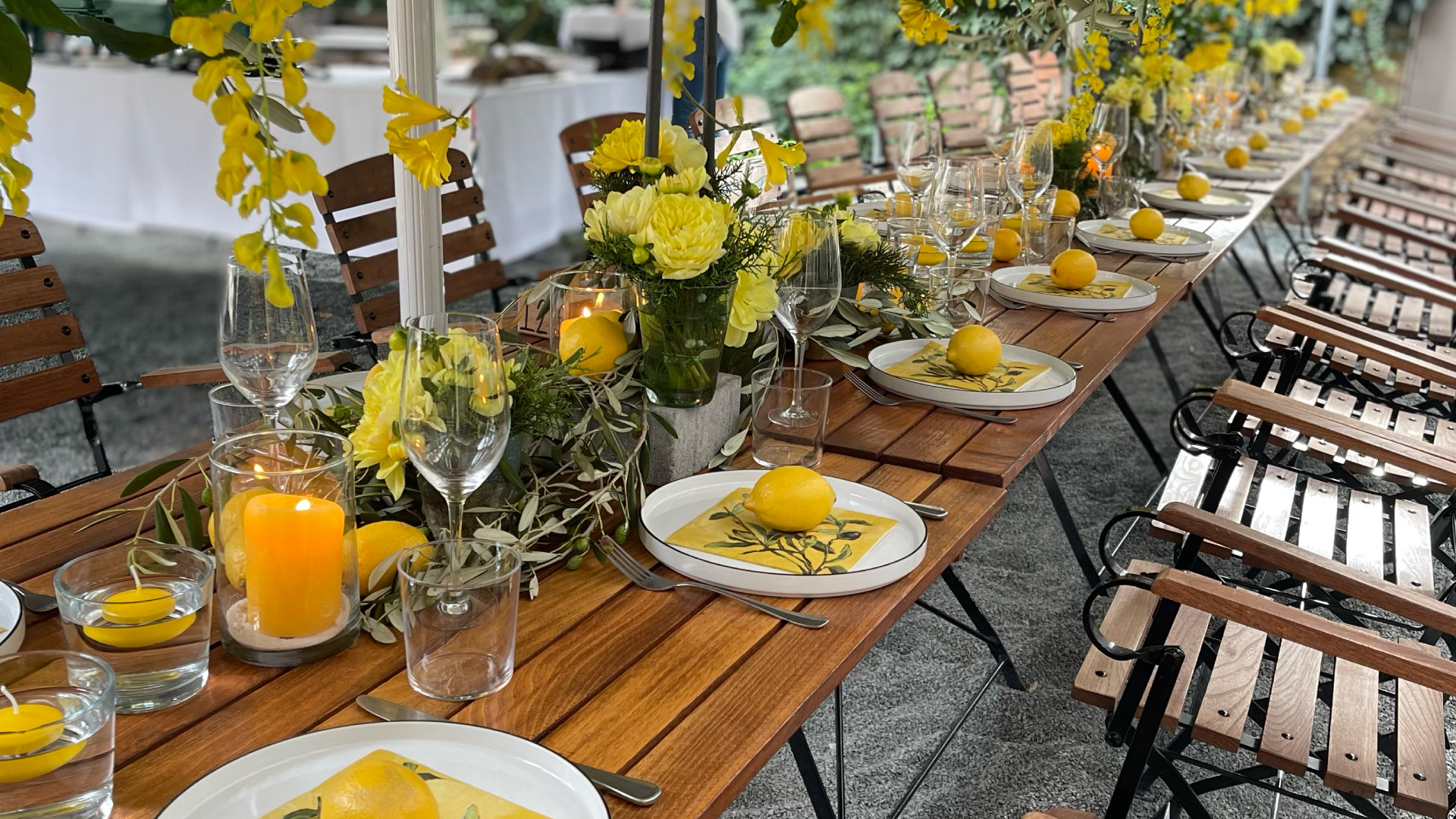 Lange Holztafel mit gelben Blumen, Zitronen auf den Tellern und Kerzen für eine Familienfeier